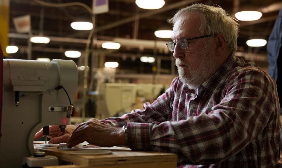  Joe Gable, an elderly man with gray hair and glasses, works intently at a sewing machine.
